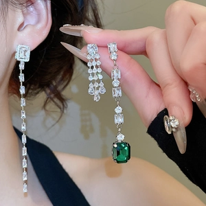 Detailed view of silver tassel earrings with clear and green zirconia on a model