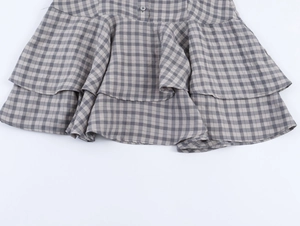 Détail d'une mini robe à carreaux à volants avec texture tissée et bouton gris