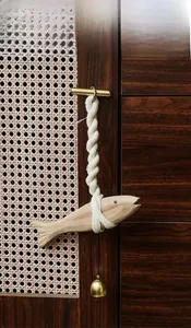 Detail of wooden fish hanging decor with thick cotton rope and small brass bell