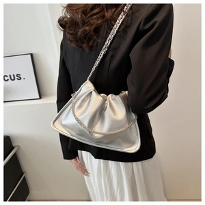 Side view of a silver ruched cloud bag with a metal chain strap on a model
