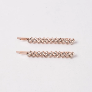 Close-up of two rose gold rhinestone hair clips with sparkling wave pattern on white background