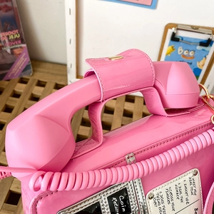 Close-up of bright pink retro telephone handbag with patent leather texture and cord handle