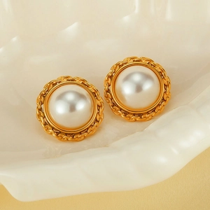 Detail of vintage gold woven earrings with central white pearl on a shell tray
