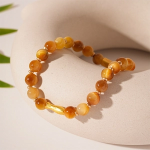 Macro detail of brown tiger eye bead bracelet featuring a gold fish-shaped metal charm