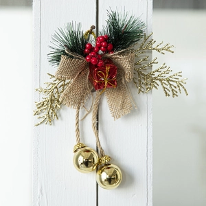 Christmas pine cone ornament with red bow, golden bells and berries on white wood
