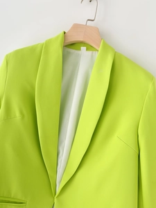 Détail d'un blazer vert vif avec revers à encoche sur un cintre en bois sur fond blanc