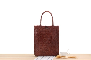 Detail of a dark brown woven straw tote bag on a wooden desk with a coffee cup