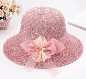 Dettaglio ravvicinato di un cappello di paglia rosa con grande fiore di organza e perle