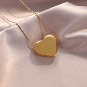 Golden heart pendant necklace on pink silk fabric with a delicate snake chain