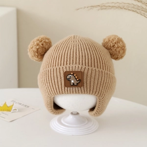 Detailed knit texture of baby earflap hat with dual pom-poms and dinosaur label