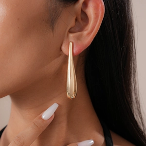 Close-up of golden teardrop earring worn by a model showcasing polished metallic texture