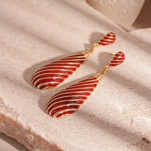Detailed view of red enamel teardrop earrings with gold zebra stripes on a stone base