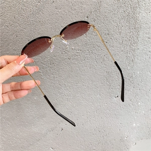 Détail de lunettes de soleil ovales sans monture avec verres dégradés bruns et branches dorées