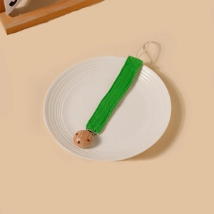 Détail de l'attache-tétine en coton vert avec clip en bois de hêtre sur plateau blanc