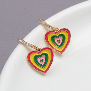 Macro detail of gold hoop earrings with colorful layered enamel heart pendants and crystals