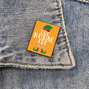 The Nurse Elf enamel pin with festive Christmas patterns on a blue denim jacket collar