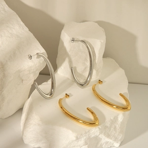 Polished gold and silver C-shaped hollow hoop earrings on a white stone background
