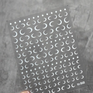 Macro shot of white crescent moon and dot nail art stickers on a textured grey background