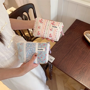 Floral fabric cosmetic pouch with zipper detail shown held by a hand for size reference