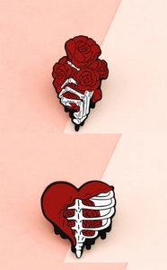 Detail of skull hand holding red roses and melting heart ribcage enamel pins
