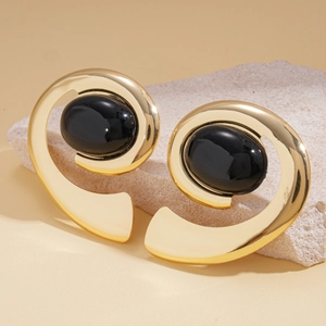 Close-up of vintage geometric spiral gold earrings with oval black stones on stone display