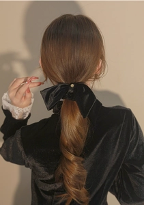 Detail of an elegant black velvet bow hair scrunchie with a gold buckle on a ponytail