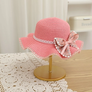Détail d'un chapeau de paille rose avec un grand nœud floral et bordure en dentelle