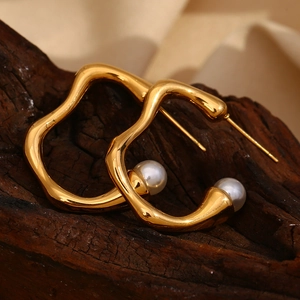 Close-up of gold irregular wave hoop earrings with white pearls on a wood background