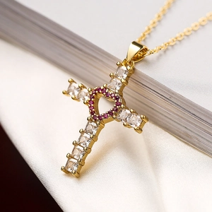 Gros plan du pendentif croix plaqué or avec zircons cubiques et détail de cœur rose