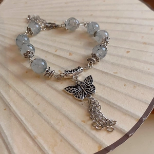 Detail of vintage beaded bracelet featuring hollow butterfly pendant and tassel accents