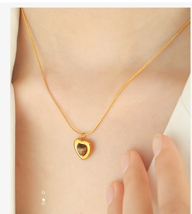 Close-up of a heart necklace with golden chain and tiger eye stone inlay on model