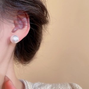 Close-up of a large white pearl stud earring worn with a beige elegant knitted top
