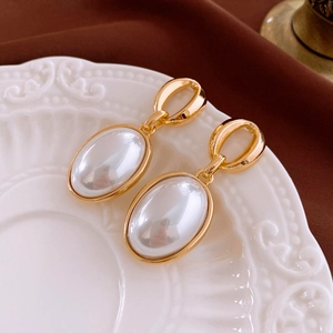 Detailed macro shot of vintage oval pearl earrings on a classic white embossed plate