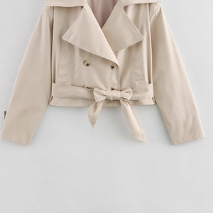 Detailed close-up of beige trench coat with double-breasted buttons and tied waist belt