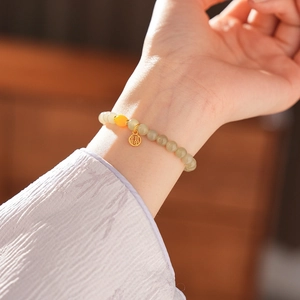 Detailed close-up of a jade bead bracelet featuring a golden Fu character charm