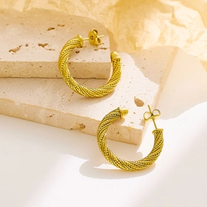 Macro shot of gold twisted rope earrings on a textured stone and beige paper background