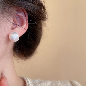 Close-up of a 10mm white pearl stud earring worn by a model in soft lighting