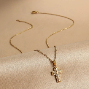 Macro shot of gold cross pendant with cubic zirconia on champagne silk texture