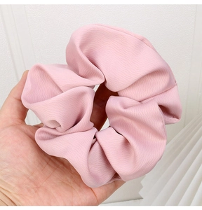 Detail of pink satin scrunchie held in hand showing soft texture and large pleats