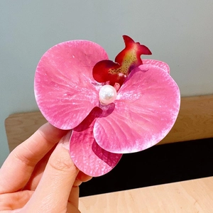 Detail of pink orchid hair clip with central pearl accent held in hand