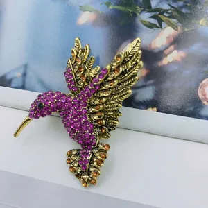 Detailed close-up of hummingbird brooch with purple and amber crystals on gold alloy