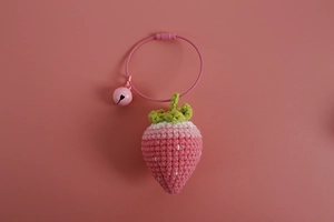 Detail of handmade crochet strawberry charm with pink gradient yarn and tiny bell