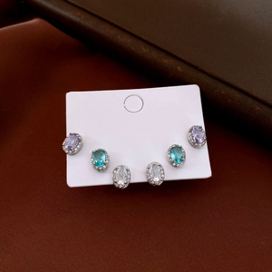 Three pairs of oval halo stud earrings in purple, blue, and clear zircon on a display card