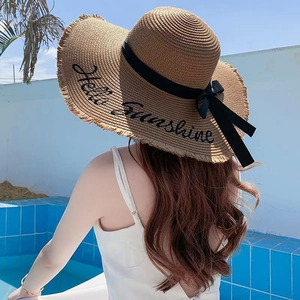 Detail of straw hat with 'Hello Sunshine' embroidery and black ribbon by a pool