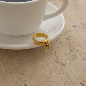 Minimalist wide gold stainless steel ring with charm on a white ceramic porcelain tray