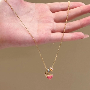 Gold-plated heart necklace with pink enamel and beads shown in a close-up hand holding view