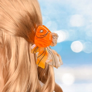 Detailed view of an orange goldfish hair claw clip with rhinestones in blonde hair