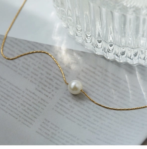 Detail shot of a minimalist single pearl pendant necklace with a fine gold chain