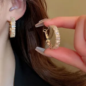 Golden hoop earrings with rectangular baguette zircons shown on ear and hand