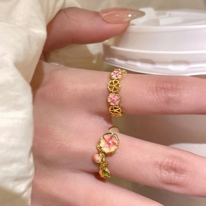 Macro shot of two floral 18k gold plated rings with pink enamel petals on a finger